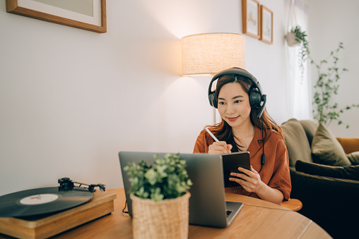 Young asian woman wearing headphones for meeting distantly at home.