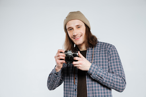 Happy hipster which holding retro camera . Isolated gray background