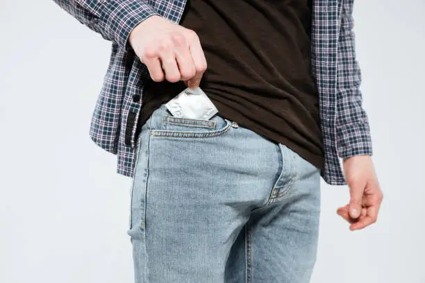 Cropped image of hipster which laying the condom in his pocket. Isolated gray background