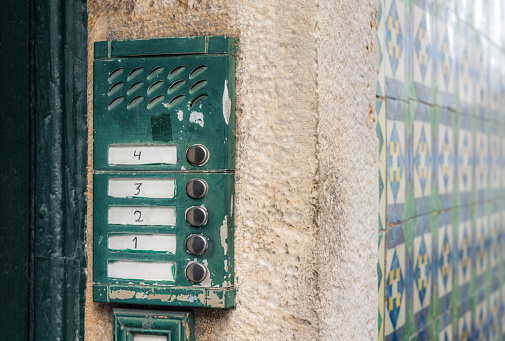 Buzzers for flats at each level outside the entrance to an old fashioned apartment building in Lisbon, Portugal, with traditional tiles making up the exterior finish of the building.