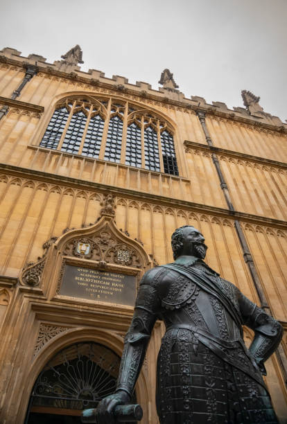 The Bodleian Library with sign in the foreground The famous Bodleian Library building in Oxford, Oxfordshire, England, UK, with a statue of William Herbert, 3rd Earl of Pembroke, in the foreground and the entrance in the background.
This bronze statue of William Herbert, 3rd Earl of Pembroke (1580–1630) stands in front of the main entrance to the Old Bodleian Library, looking east across the Schools Quadrangle.

It is Grade II listed, weights about 1600 lb, and was sculpted by Hubert Le Sueur It orginally stood in the family seat of Wilton House in Wiltshire.

In 1723 the 8th Earl of Pembroke transferred the statue to the Bodleian Library from the family home at Wilton in Wiltshire. Originally it stood indoors in the Bodleian Picture Gallery on the third floor. earl of pembroke stock pictures, royalty-free photos & images