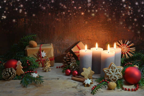 Fourth Advent, four candles are lighted, Christmas decoration and gifts on rustic wooden planks against a dark brown background with copy space, selected focus stock photo