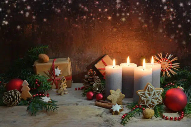 Fourth Advent, four candles are lighted, Christmas decoration and gifts on rustic wooden planks against a dark brown background with copy space, selected focus, narrow depth of field
