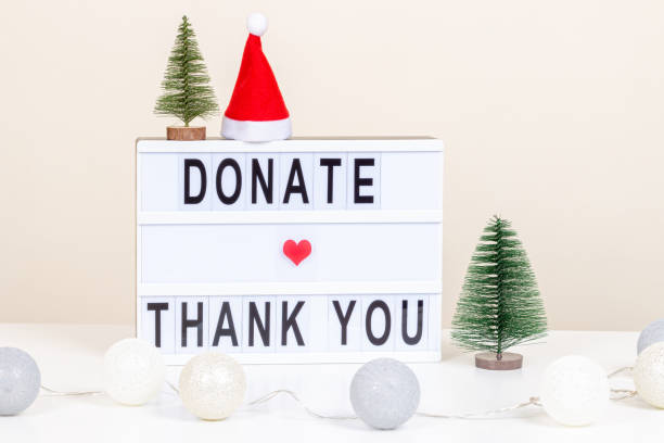 donazione di natale, beneficenza. dona e ringrazia il messaggio su lightbox. decorazione natalizia e ghirlanda su scrivania bianca. vista frontale, primo piano - gift charity and relief work giving human hand foto e immagini stock