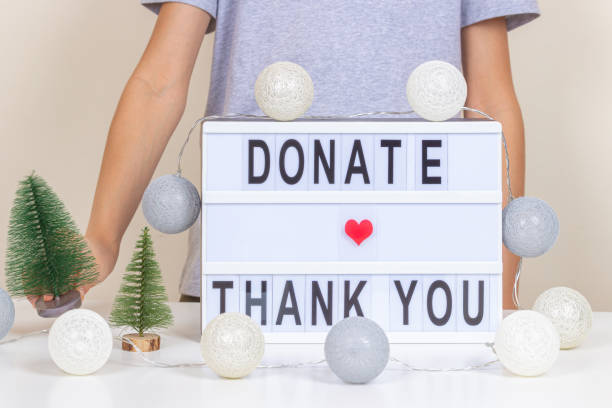 christmas donation, charity. kid standing near desk with light box and christmas decoration. donate and thank you message on lightbox. front view, close up - charity and relief work donation box thank you child imagens e fotografias de stock