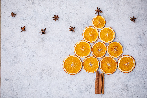 Christmas tree made of slices of dried oranges, cinnamon sticks and star anise on a gray background.