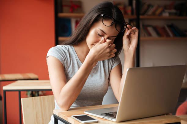 Femme fatiguée à l’intérieur en utilisant un ordinateur portable et en se touchant le nez. - Photo