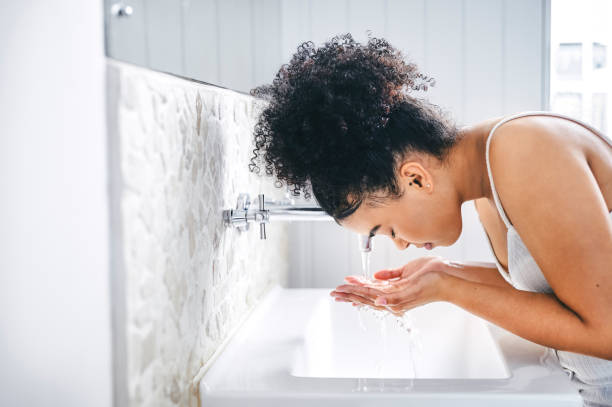 scatto di una giovane donna che si lava il viso nel lavandino del bagno - lavarsi il viso foto e immagini stock