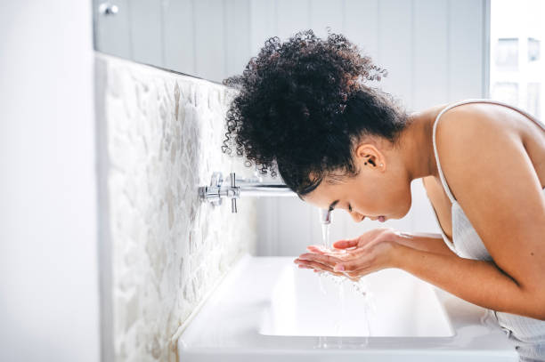 shot of a young woman washing her face in her bathroom basin - gezicht wassen stockfoto's en -beelden