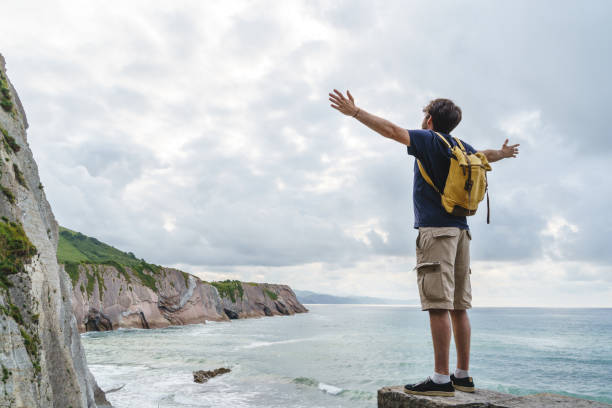 istock Panoramic view of unrecognizable man with arms wide open in a cliff. 1352302581