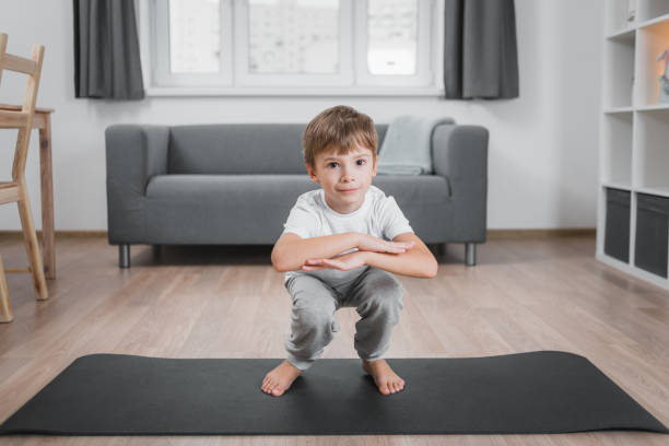 Boy-child doing classic squats at home on the floor on a sports mat, wearing a white t-shirt and gray pants. Boy-child doing classic squats at home on the floor on a sports mat, wearing a white t-shirt and gray pants ass boy stock pictures, royalty-free photos & images