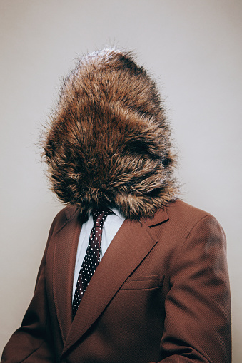 A businessman wearing a retro brown blazer has his head completely covered by fur or hair.  A bizarre humor portrait, or a nod to Movember (no shave November).