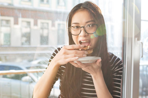 istock Asian woman eating cake on windowsill 1352304174