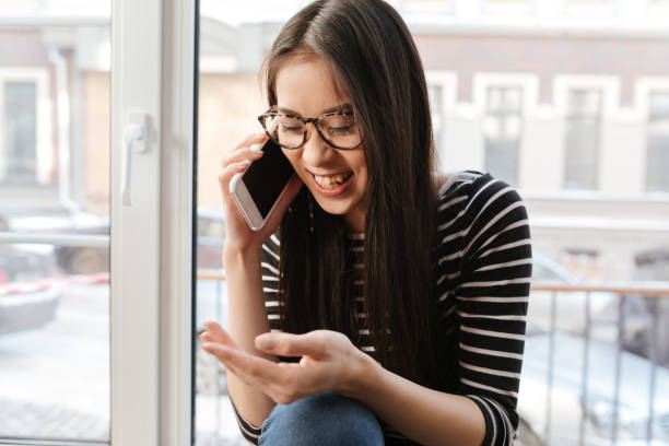 istock Happy Asian woman talking phone on windowsill 1352304874