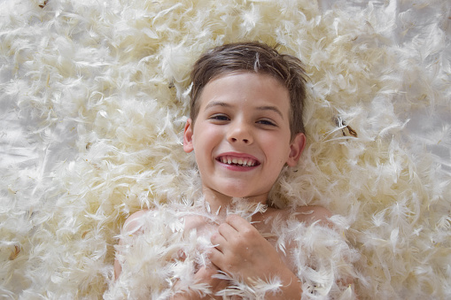 Happy boy portrait after a pillow fight with a mess in the bedroom
