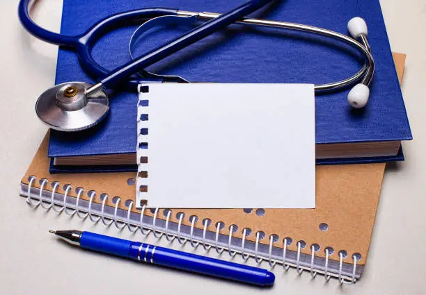 Photo of On the table are notepads, a stethoscope, a pen and a sheet of paper with space to insert text. Medical concept