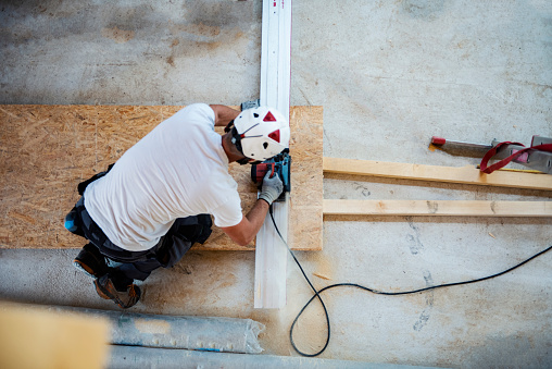 Construction worker cutting a plank with an electric saw. Top view of male carpenter at construction site. Men working with wood plank.