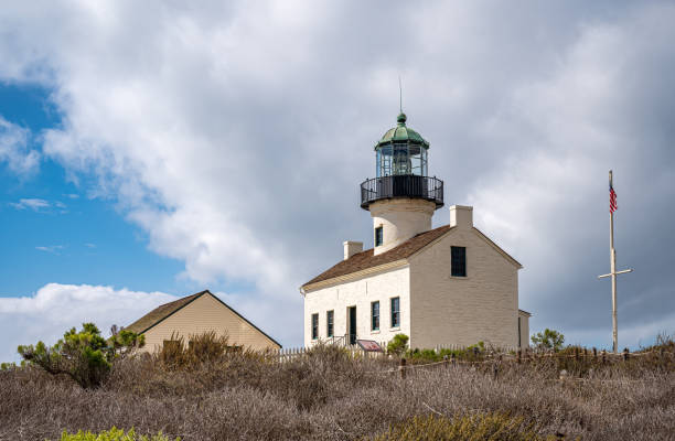 San Diego, California, USA - October 5, 2021: Cabrillo National Monument. Closeup of Old Point Loma Lighthouse on top of green vegetation hill under heavy blue cloudscape.