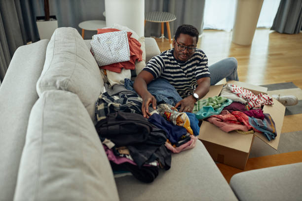 istock Young man putting clothes into a donation box at home 1352314607
