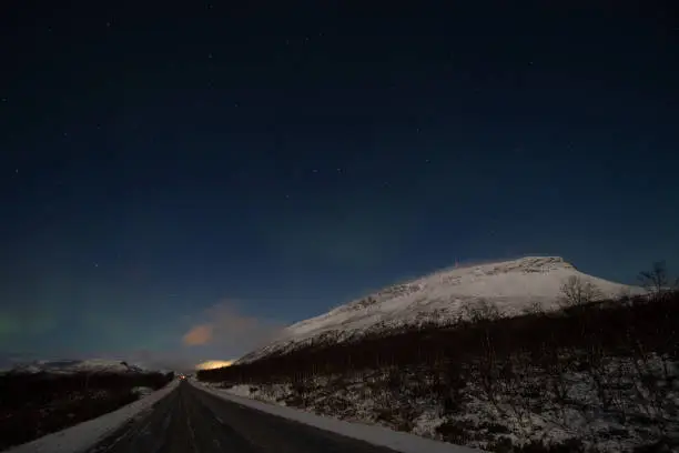 Borealis aurora sweeps over a main road on a cloudless night in Kilpisjarvi, Lapland, Finland. aurora polaris in green dances across the sky. Scandinavian magic. Saana mountain.