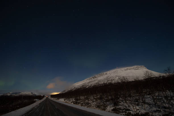 borealis aurora sweeps over a main road on a cloudless night in kilpisjarvi, lapland, finland. aurora polaris in green dances across the sky. scandinavian magic. saana mountain - saana imagens e fotografias de stock