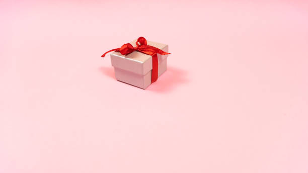 istock Small gray gift box tied with a red ribbon with a present for a loved one isolated light pink pastel background. 1352326224
