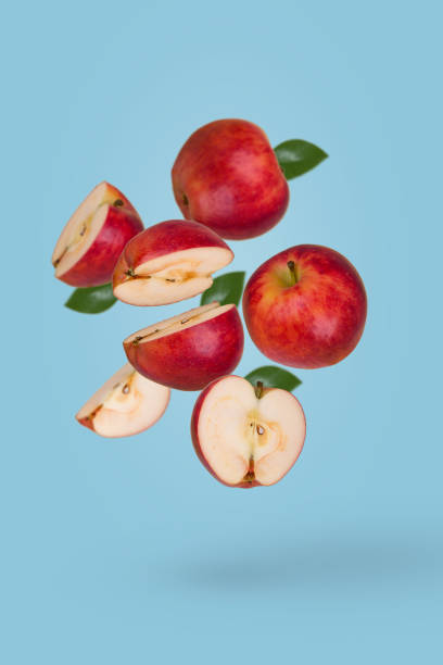 istock Minimal fruit concept with fresh sliced and whole apple floating in the air isolated on blue background. 1352332916