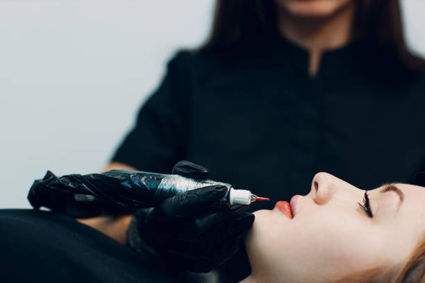 istock Cosmetologist applying red permanent make up tattoo on young woman lips. Permanent lips tattoo procedure concept. 1352346755