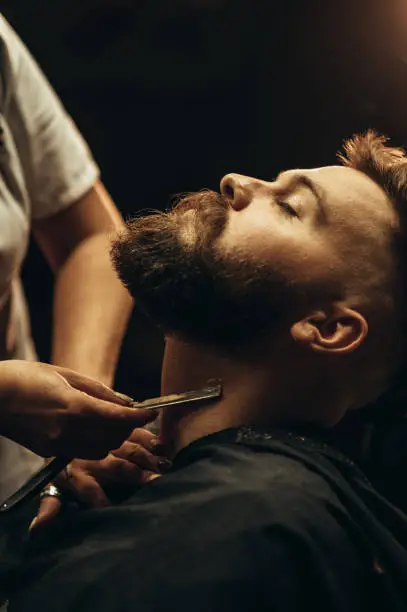 Photo of Man getting shaved with straight edge razor by hairdresser at barbershop