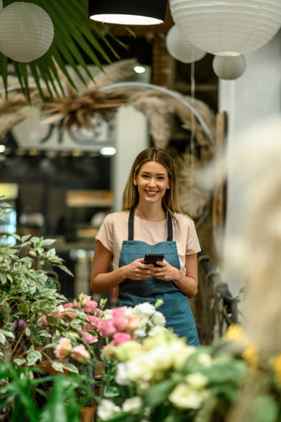 istock Florist using smartphone while surrounded with flowers and plants in a flower shop 1352346856