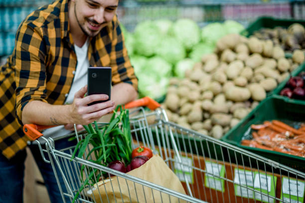 istock Young handsome man in a supermarket using smartphone while grocery shopping 1352346872