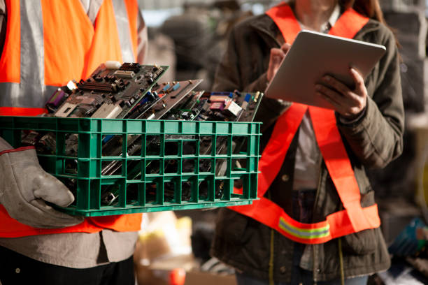 Male and female recycling worker using digital tablet while holding box full of old mother boards stock photo