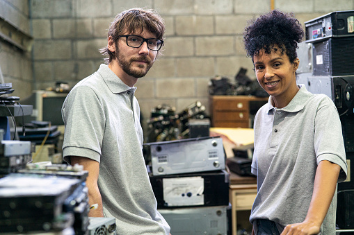 Medium shot of male and female warehouse worker looking and smiling a the camera while standing in computer recycling plant