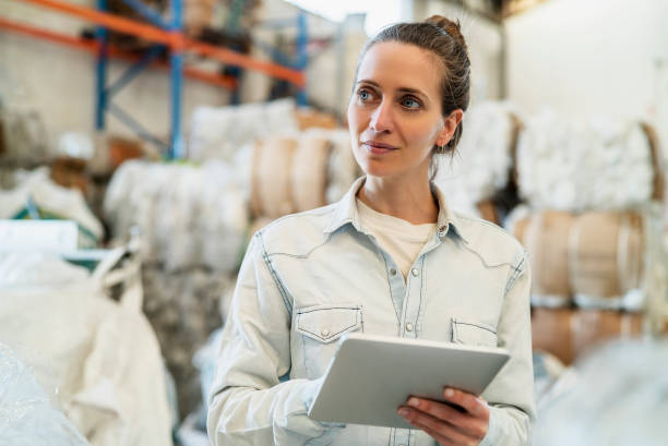 istock Portrait of smiling female worker holding digital tablet while standing inside recycling centre during daytime 1352364285