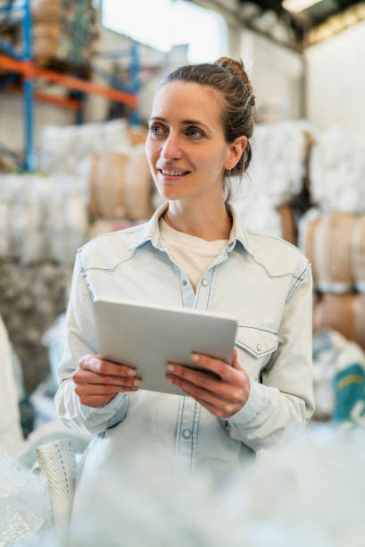 istock Portrait of smiling female worker holding digital tablet while standing inside recycling centre during daytime 1352364288
