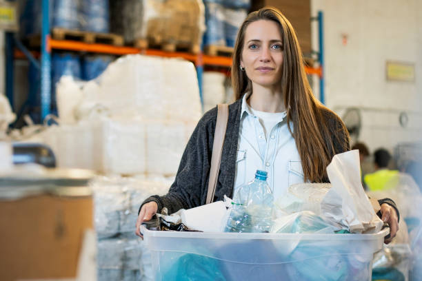 Smiling woman carrying container with plastic classified garbage at recycling centre