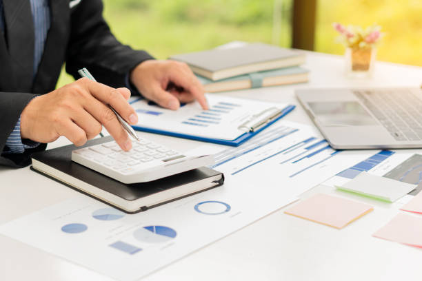 un homme d’affaires ou un comptable tient un stylo et appuie sur une calculatrice pour calculer les informations commerciales. document graphique de comptabilité financière et ordinateur portable dans le bureau de l’entreprise. - planning secretary finance business photos et images de collection