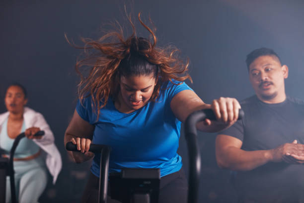 photo d’une jeune femme s’éventant avec un vélo d’exercice dans un gymnase - spinning instructor exercising gym photos et images de collection