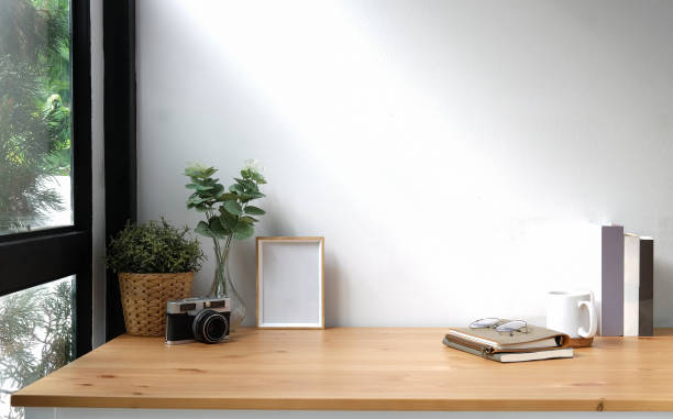 istock Creative workspace with blank poster frame, camera, coffee cup and houseplant on wood table. 1352381194