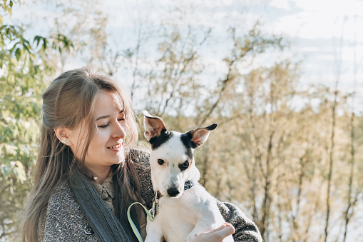 joven mujer sonriente con atuendo de otoño sosteniendo a su perro y abrazándolo. abrazando a una mascota amorosa en un parque. vista lateral del propietario y jack russell terrier en un paseo juntos. photo