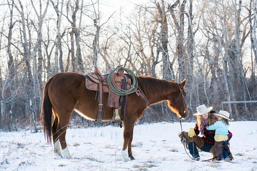 Attractive cowgirl and her toddler daughter with a quarter horse on a ranch in winter, Livingston, Montana