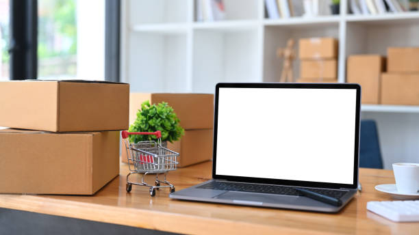 istock Laptop computer, trolley and cardboard boxes on wooden table. Online shopping or ecommmerce concept. 1352385737