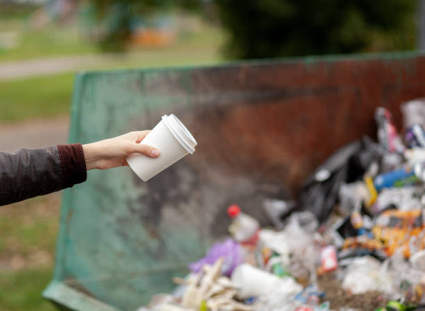 istock Woman throwing a cardboard glass into a recycling bin. large trash bin 1352387855