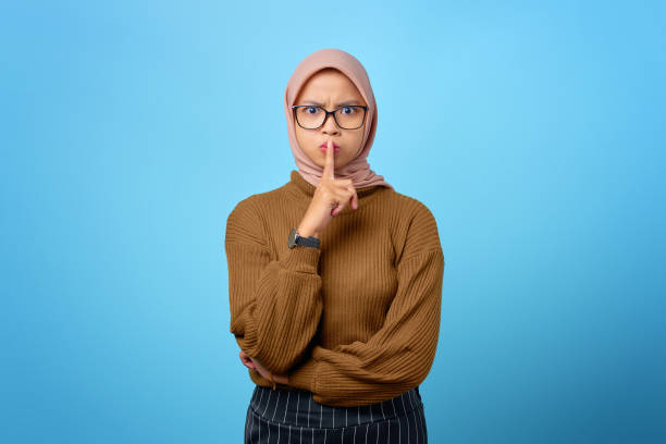 istock Attractive young Asian woman finger on lips and making silent gesture on blue background 1352394573