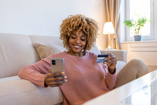 Safe mobile banking. Smiling african lady client hold mobile phone credit bank card do online shopping provide internet payment. Happy young woman enjoy easy fast secure transferring money in ebank app