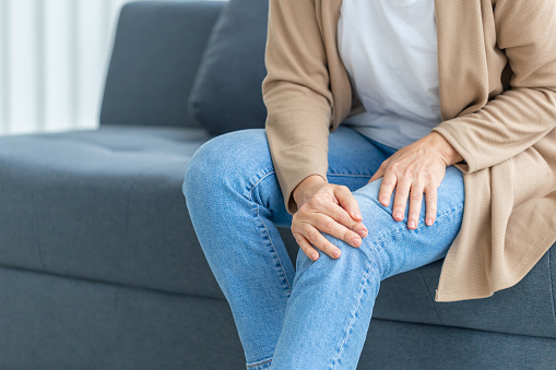 Mujer que sufre de dolor de rodilla sentado sofá en la sala de estar, mujer madura que sufre de dolor de rodilla mientras está sentada en el sofá photo