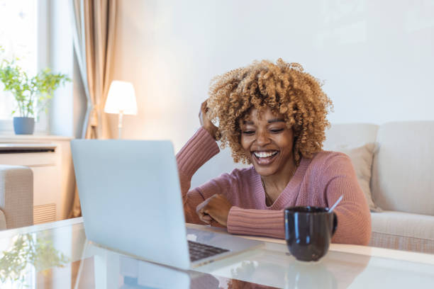 Young woman using laptop at home. Young woman using laptop at home. Young black beautiful woman using laptop at home. Young woman working at home, typing on laptop. Cropped shot of a woman using her laptop on a white table small business saturday stock pictures, royalty-free photos & images