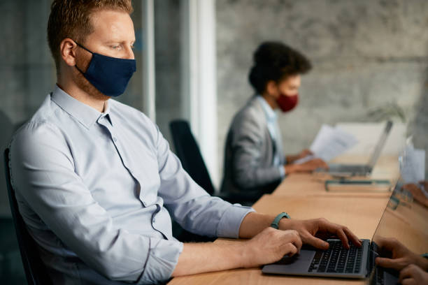 istock Businessman with protective face mask working on laptop in the office. 1352400110