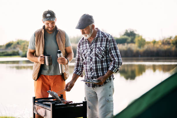 istock Senior man and his son grilling fish on barbecue while camping by the lake. 1352400723