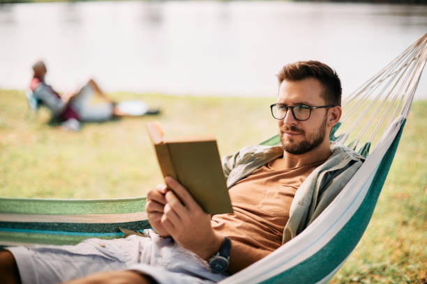 istock Mid adult man reading book while relaxing in hammock in nature. 1352400724